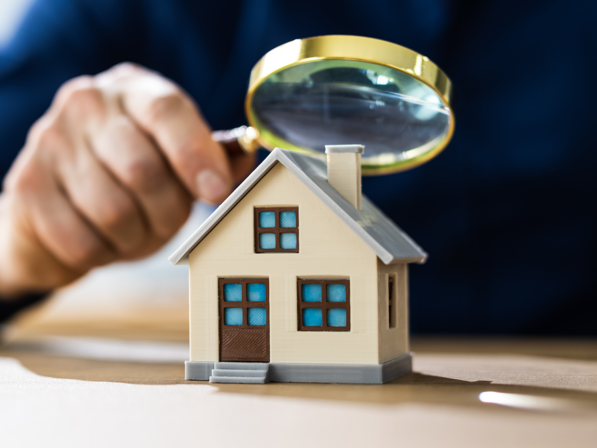 A men is holding a magnifying glass over a house doodle. Real estate home appraisals.